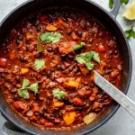 Sweet potato, black bean, quinoa chili in a pot with serving spoon on table