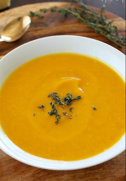 Butternut squash soup in a white bowl on a table with spring of fresh herbs