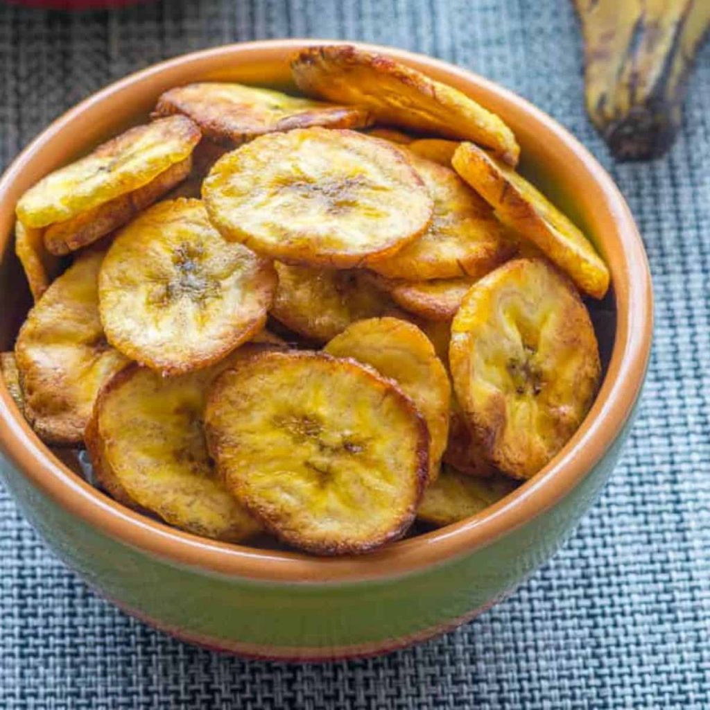 Baked plantain chips in bowl on blue tablecloth