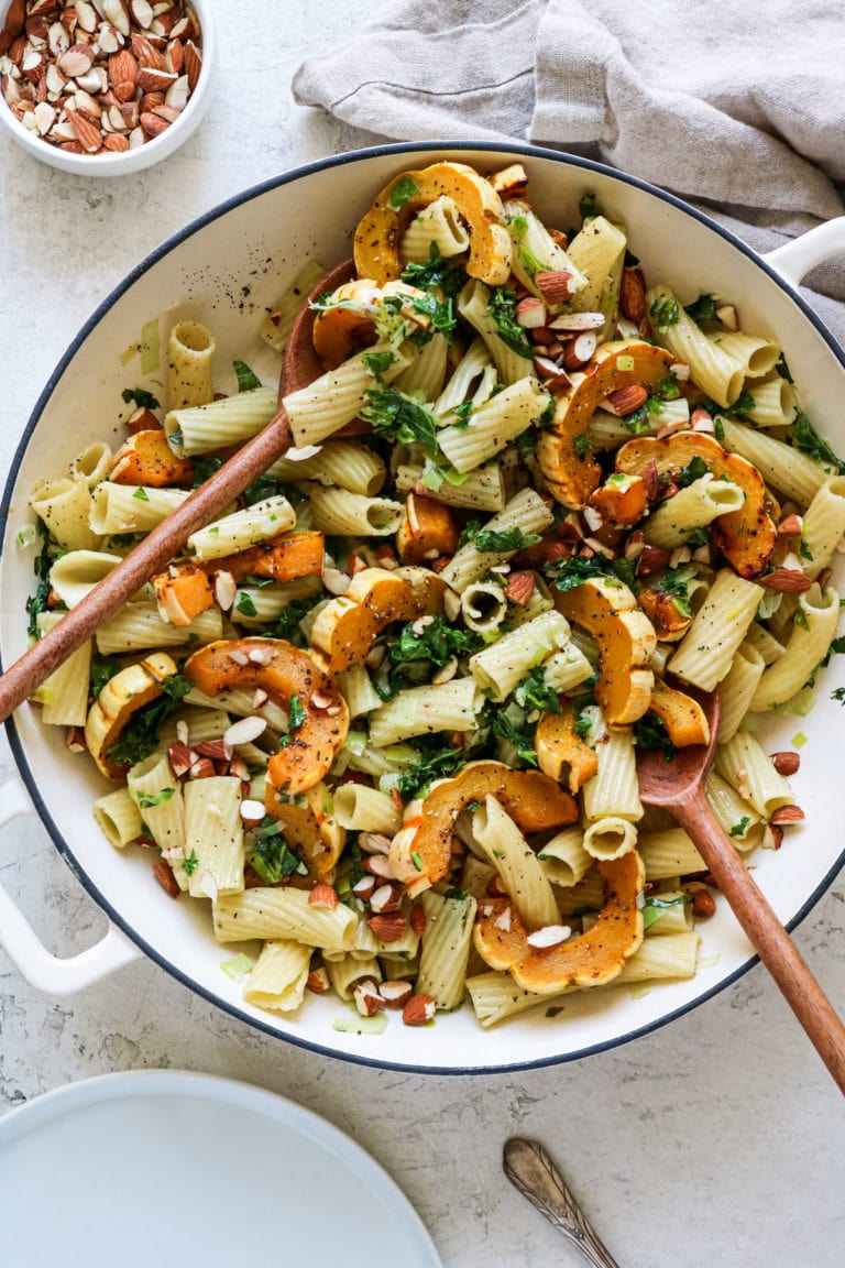 Delicata squash with pasta and kale in large bowl with serving spoons