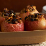 Baked red apples stuffed with oats in a baking pan with plates in the background on a table