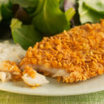 Baked flaked fish with tartar sauce on white plate with mixed greens