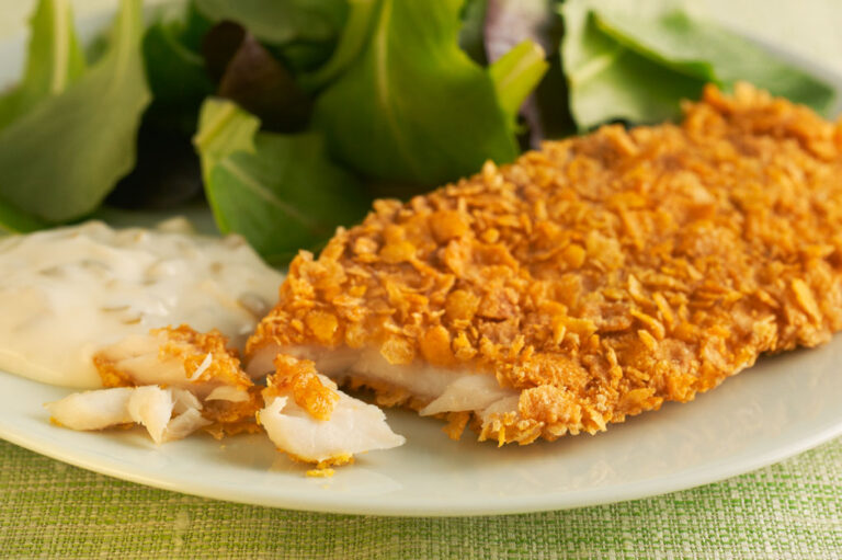 Baked flaked fish with tartar sauce on white plate with mixed greens