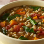 Barley and lentil soup in a white bowl on a red and white tablecloth