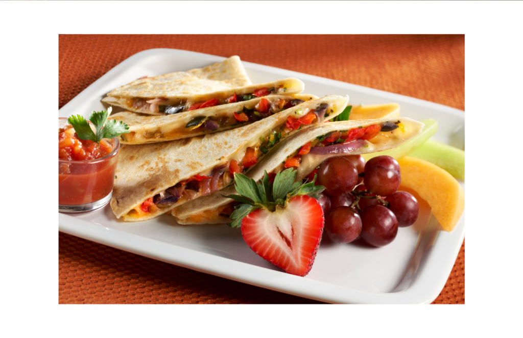 Black bean and vegetable quesadillas on white plate with sliced fruit