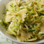 Bow tie pasta with zucchini sauce in a white dish pictured on a white tablecloth