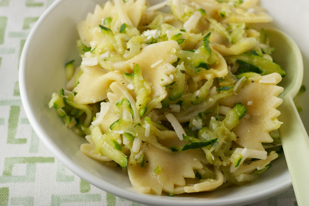 Bow tie pasta with zucchini sauce in a white dish pictured on a white tablecloth