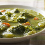 Broccoli soup in a white bowl pictured on a white tablecloth