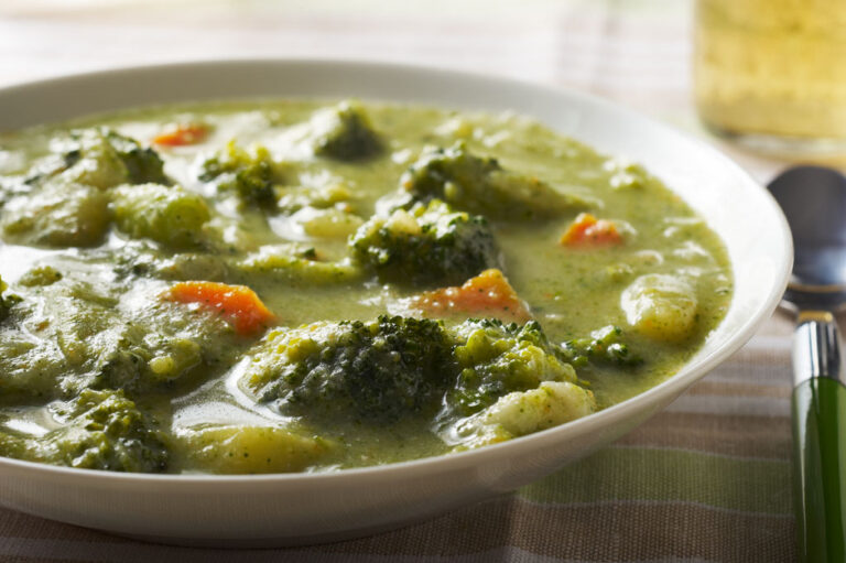 Broccoli soup in a white bowl pictured on a white tablecloth