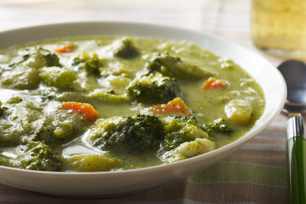 Broccoli soup in a white bowl pictured on a white tablecloth