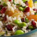 Brown rice and orange salad pictured on a blue plate on top of a white tablecloth