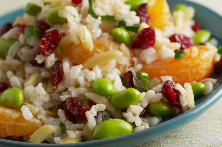 Brown rice and orange salad pictured on a blue plate on top of a white tablecloth