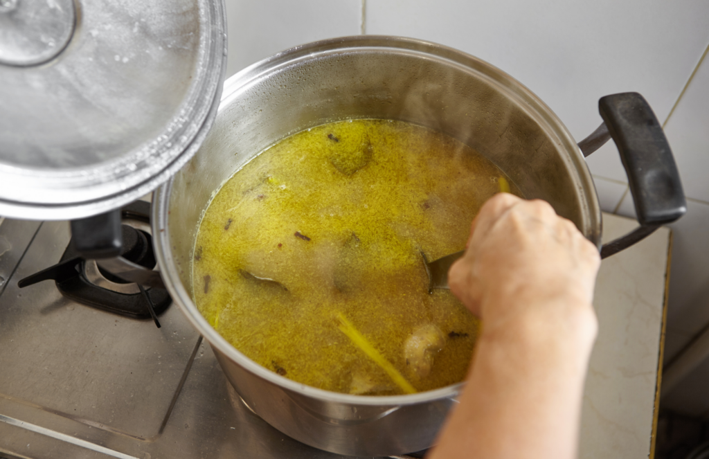 Chicken stock and metal pot on stove with a hand stiring