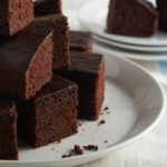 Chocolate cake on a white plate on top of a white and blue tablecloth