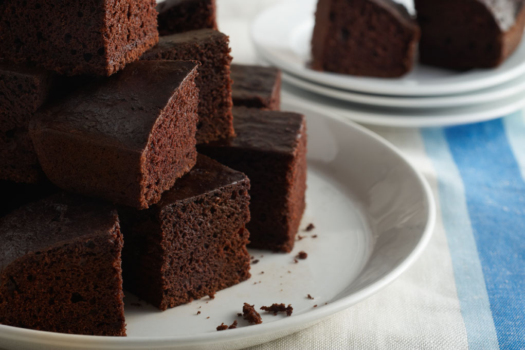 Chocolate cake on a white plate on top of a white and blue tablecloth