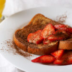 Chocolate strawberry French toast on a white plate with strawberries.