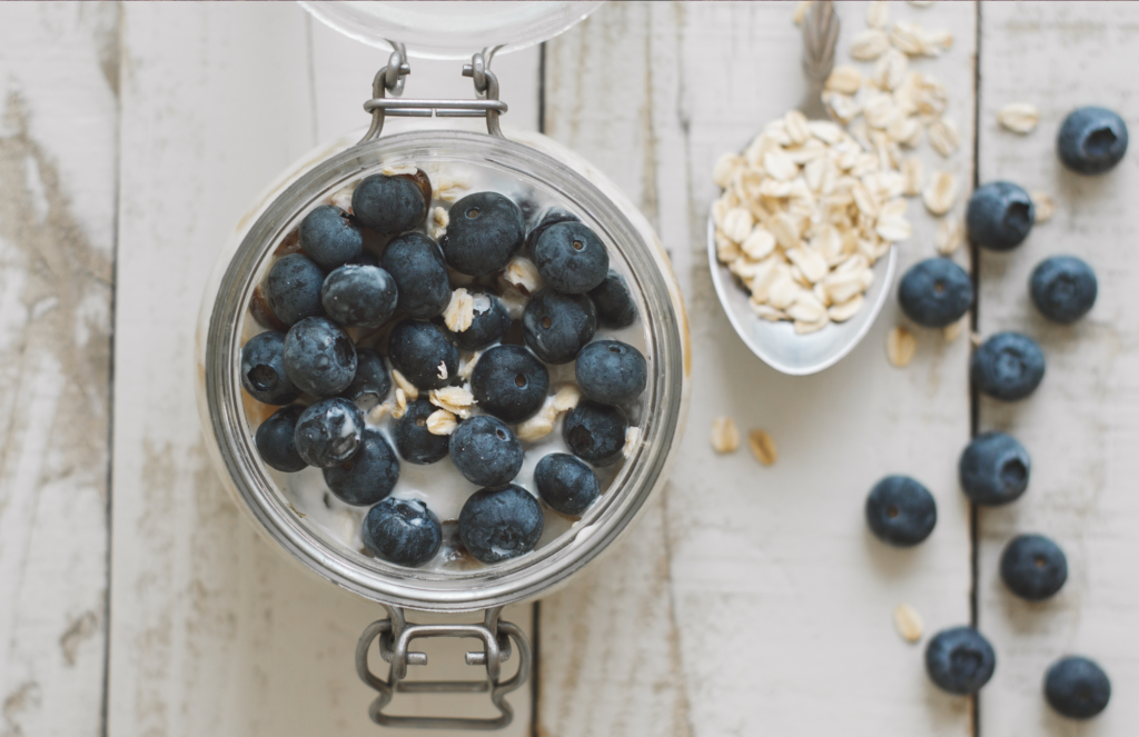 Overnight oats in a mason jar on a wooden table. Blueberries top the oats and are scattered on the table.
