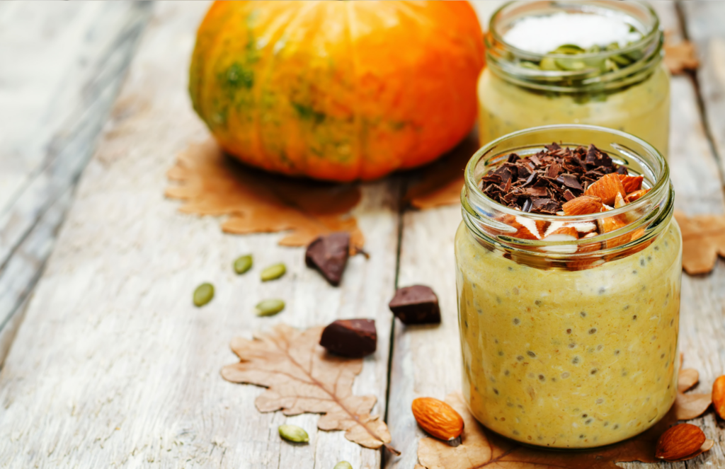Overnight oats in a mason jar on a table with leaves, chocolate bits, and a pumpkin.