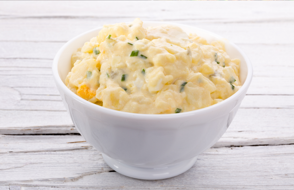 Rutabaga (no potatoes) Potato Salad in a white bowl on a grey wooden table.