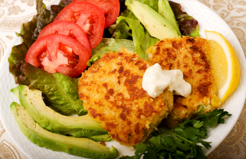 Salmon cakes with creamy dill sauce on a bed of lettuce with avocado, tomato, and lemon.