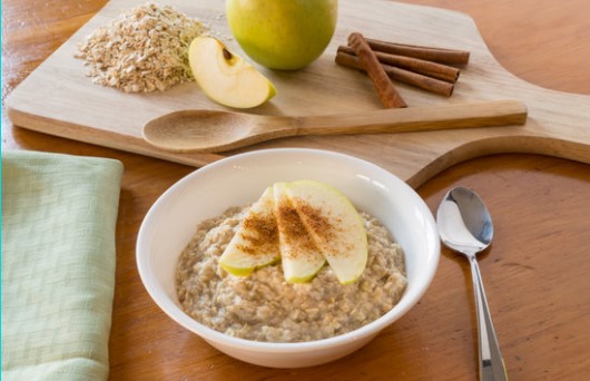 Apple Cinnamon Oatmeal in a bowl with spoon and cutting board with apple and cinnamon sticks in the background