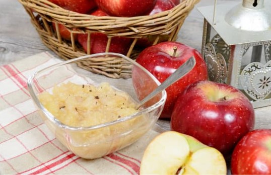 Applesauce with red apples on a a red and white tablecloth with apples in a basket.