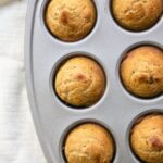 Applesauce muffins in a muffin tin on a white tablecloth.