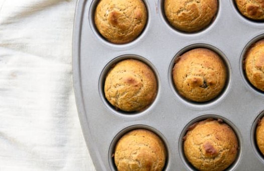 Applesauce muffins in a muffin tin on a white tablecloth.
