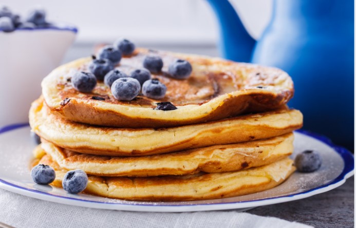 Blueberry pancakes on a white and blue plate with a blue pitcher.