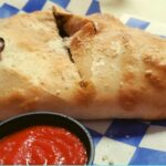 Breakfast stromboli with mushroom on a blue and white check tablecloth with a side of ketchup.