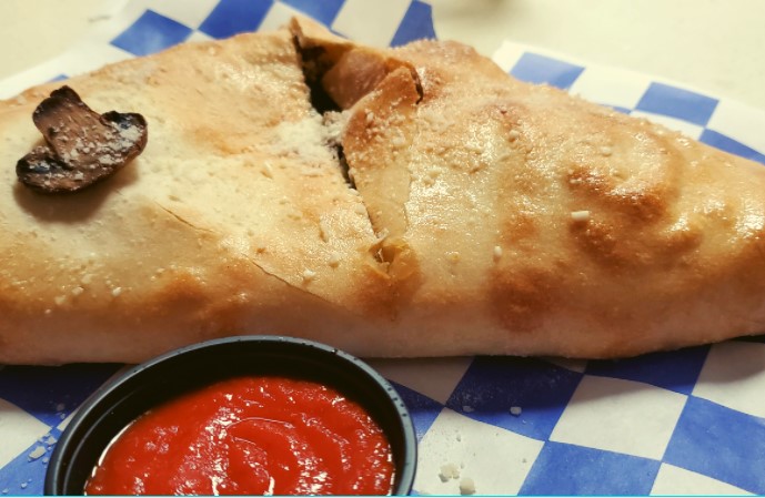 Breakfast stromboli with mushroom on a blue and white check tablecloth with a side of ketchup.