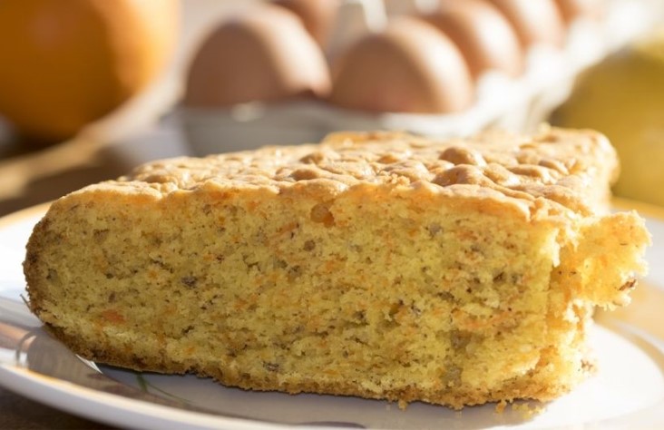 Carrot cake slice on a white plate with eggs in the background.