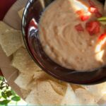 Cheesy Dip Bean with tomatoes and tortilla chips on a white plate on top of a wooden table.