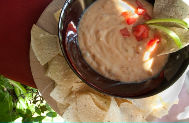 Cheesy Dip Bean with tomatoes and tortilla chips on a white plate on top of a wooden table.