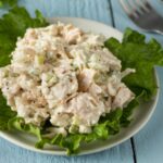 Chicken salad on top of lettuce on white plate with fork in the background on blue wooden table