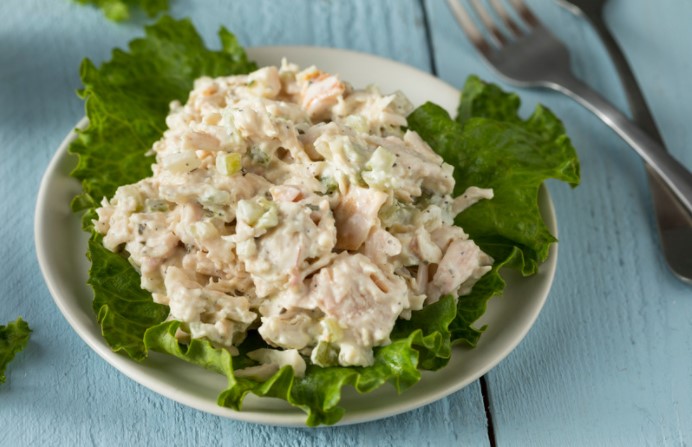 Chicken salad on top of lettuce on white plate with fork in the background on blue wooden table