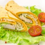 Chicken wraps with corn tortillas, on a bed of lettuce with fresh tomatoes.