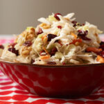 Cranberry walnut coleslaw in a red bowl pictured on a red and white tablecloth