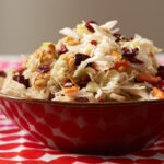 Cranberry walnut coleslaw in a red bowl pictured on a red and white tablecloth