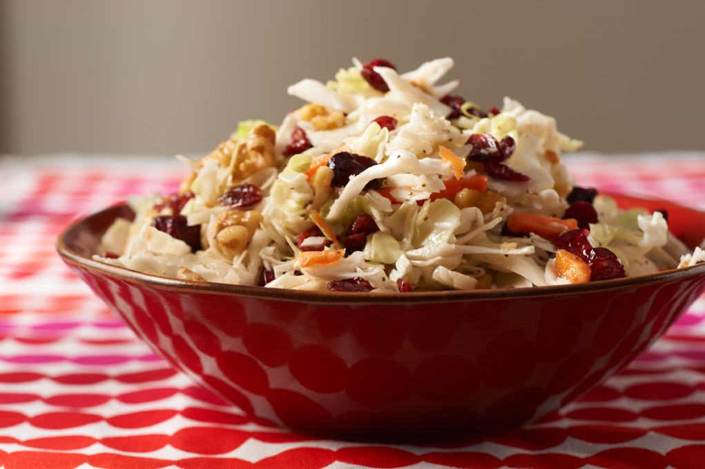 Cranberry walnut coleslaw in a red bowl pictured on a red and white tablecloth