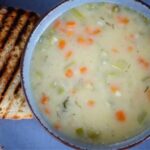 Creamy vegetable soup in a blue bowl with a slice of toasted bread.