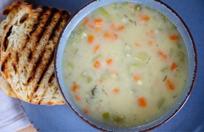 Creamy vegetable soup in a blue bowl with a slice of toasted bread.