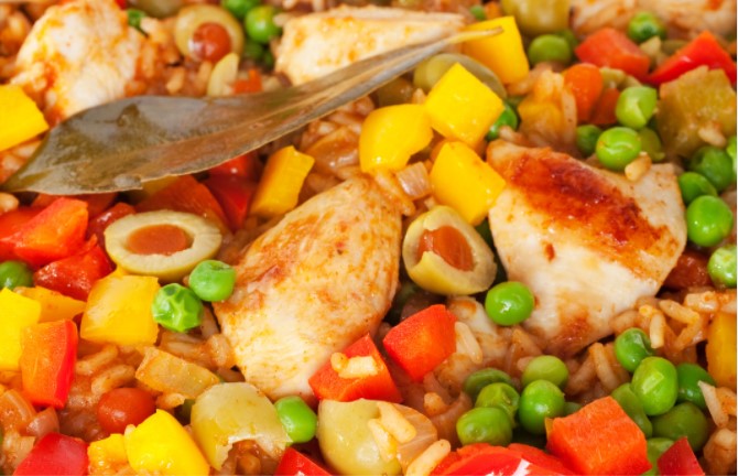 Closeup photo of a Cuban dish which includes chicken, green olives, peas, chopped carrots, and rice