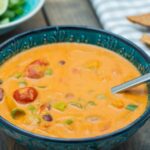 Coconut, tomato curried soup in a blue bowl with a spoon, tortilla chips and a blue and white checked napkin.