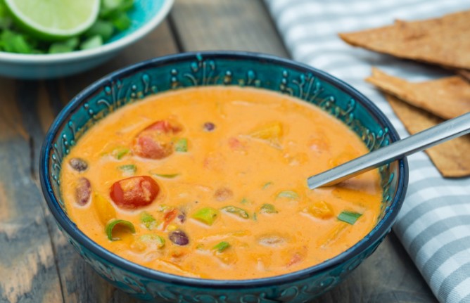 Coconut, tomato curried soup in a blue bowl with a spoon, tortilla chips and a blue and white checked napkin.