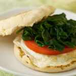 English muffin breakfast sandwich on a white plate.