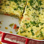 A freshly baked frittata in a red and white baking dish sits atop a white kitchen towel