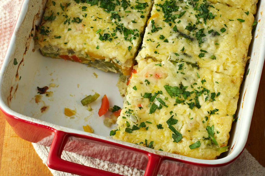 A freshly baked frittata in a red and white baking dish sits atop a white kitchen towel