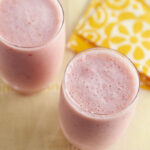 Fruit smoothies placed on a table near a yellow and white tablecloth.