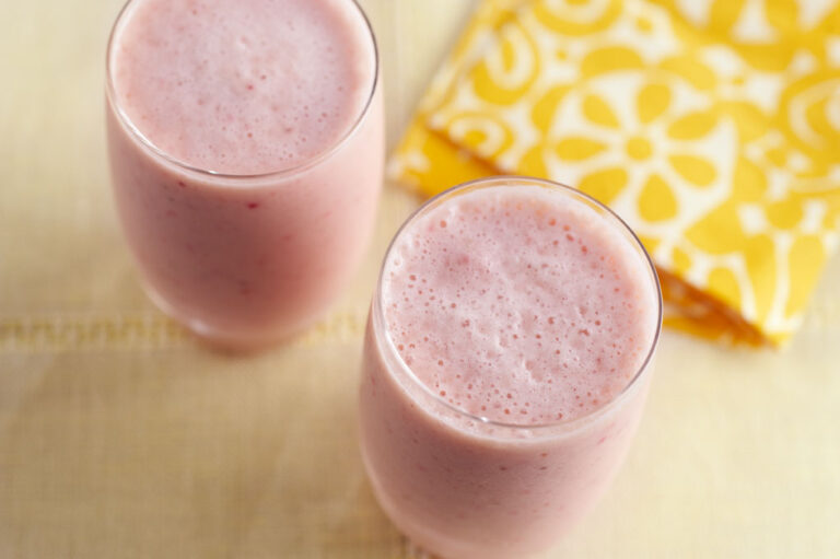 Fruit smoothies placed on a table near a yellow and white tablecloth.